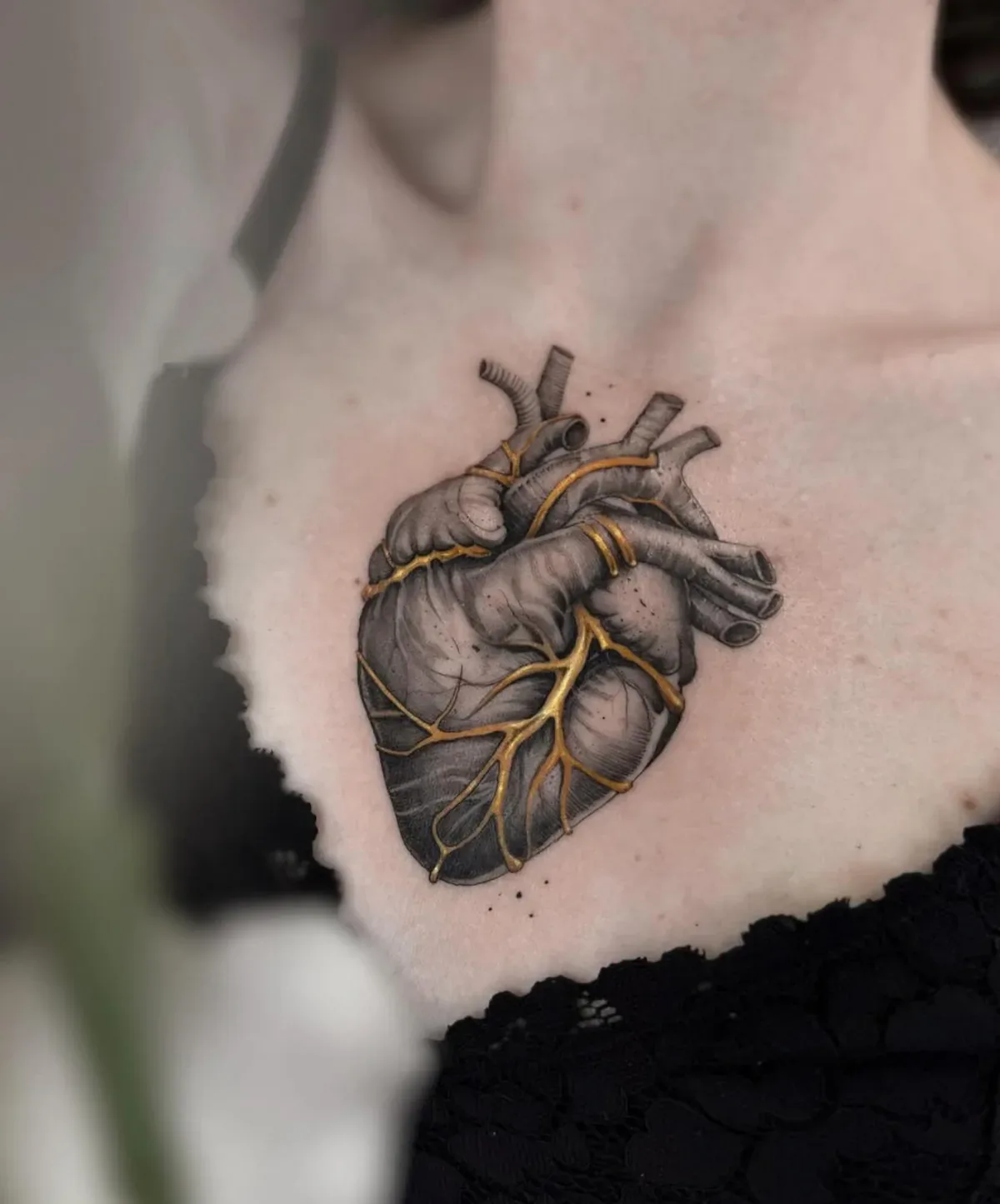 Anatomisches Herz mit goldenen Adern auf der Brust. Black-and-Grey-Tattoo mit Goldakzenten von Annlie.